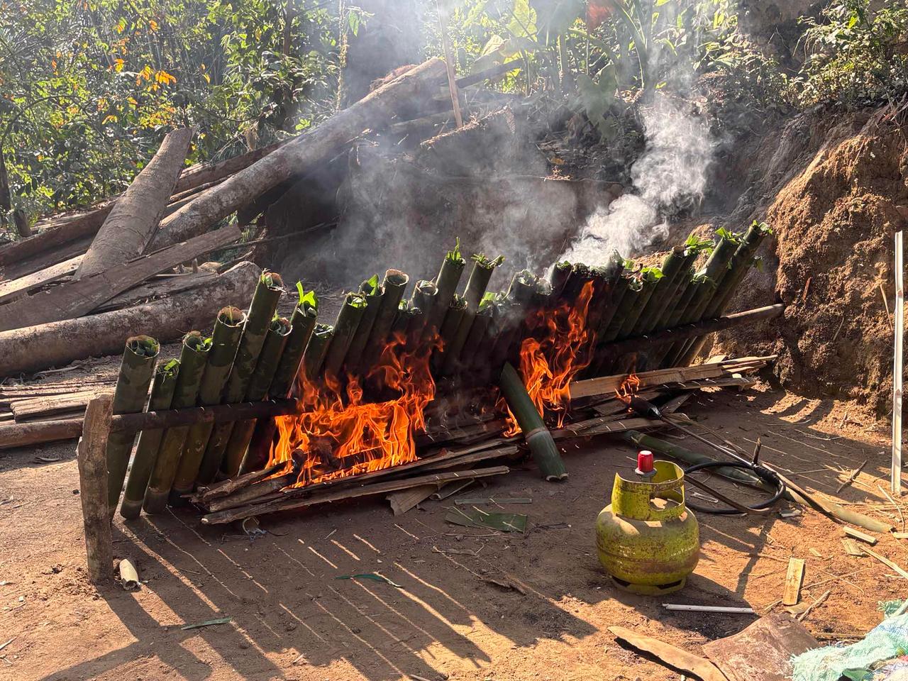 Rows of bamboo tubes filled with meat set alight over an open fire