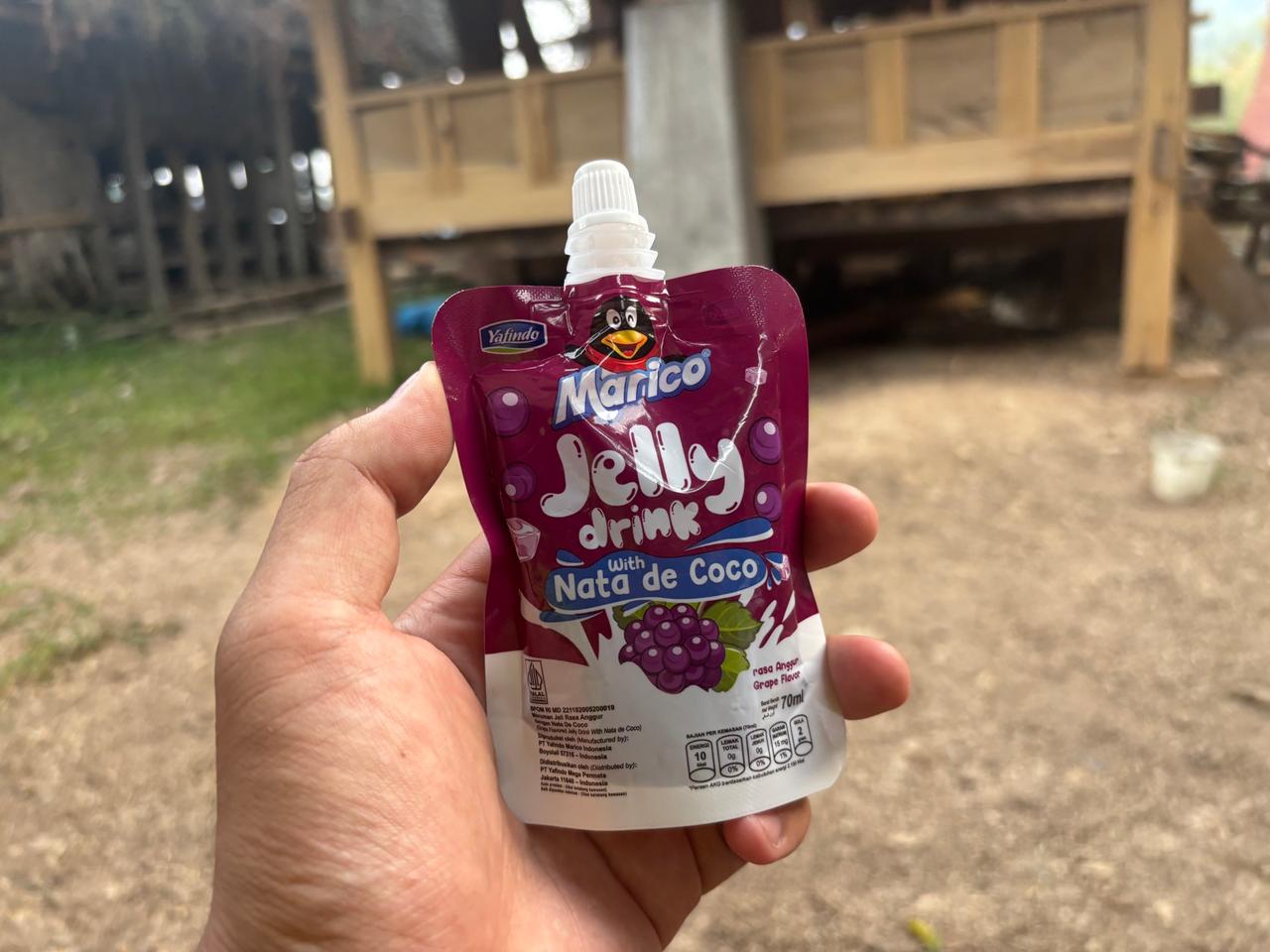 A hand holding a grape-flavored jelly drink pouch with nata de coco