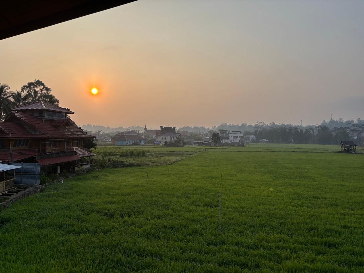 A hazy orange sunrise over Torajan rooftops and rice fields