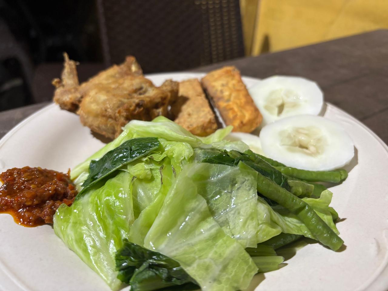 A plate of fried tempeh, boiled cabbage, cucumber and sambal at a local diner