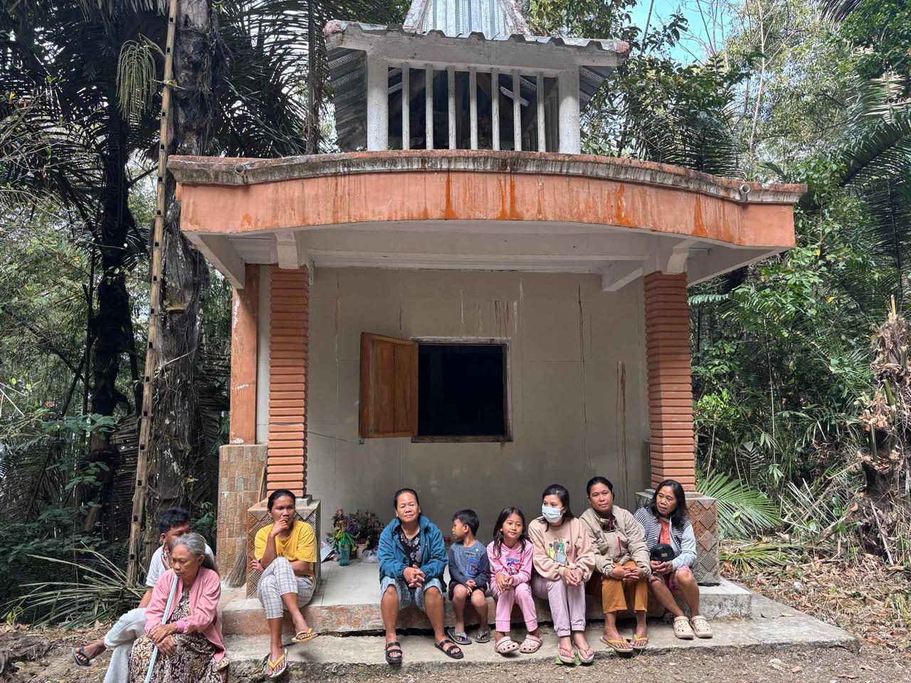 Family members sitting together in front of a mausoleum, waiting quietly