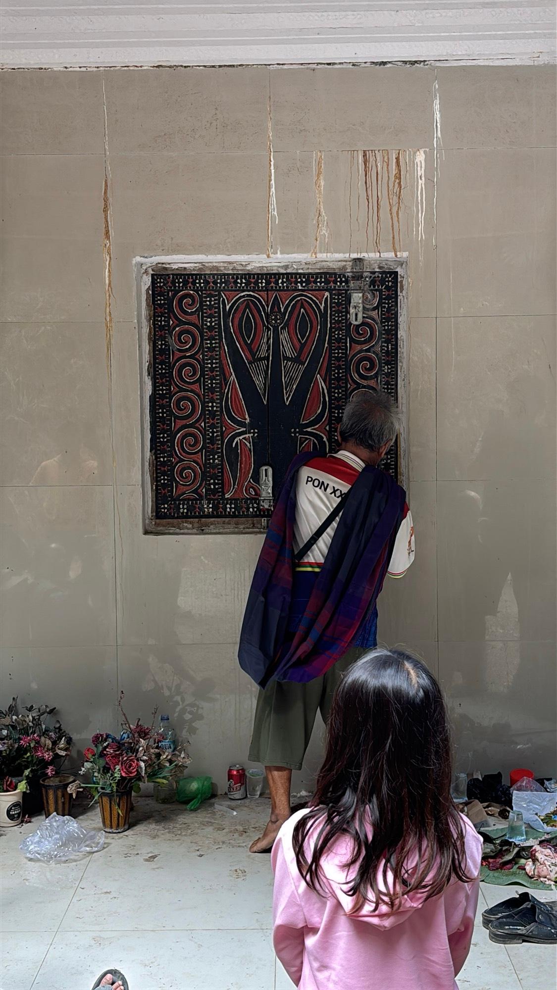An elderly man closing the ornately painted wooden doors of a family crypt
