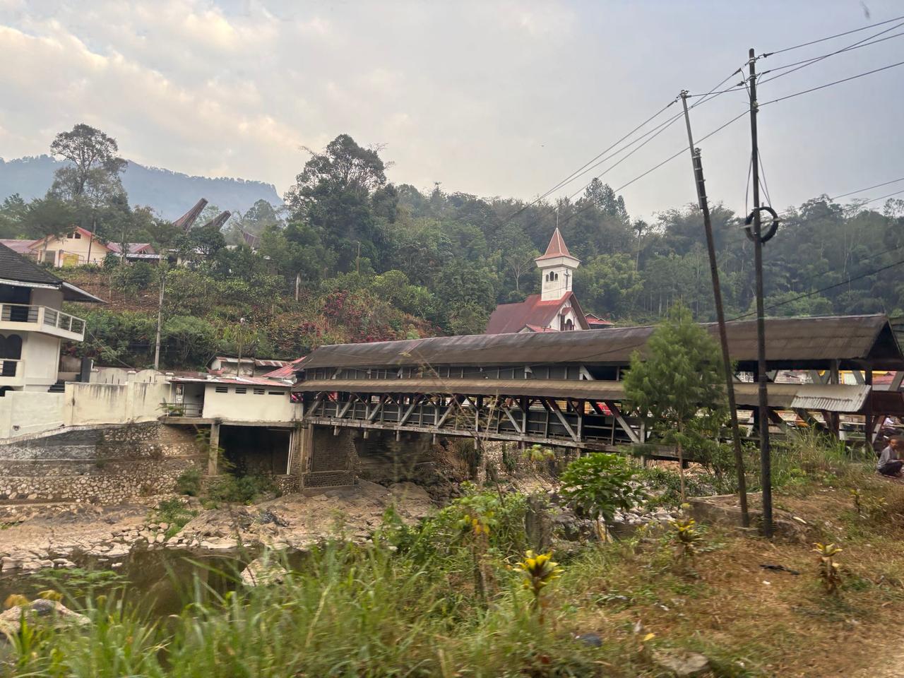 A river-side village in Rantepao at dawn, with a church steeple and traditional Torajan roof peaks visible in the misty hills
