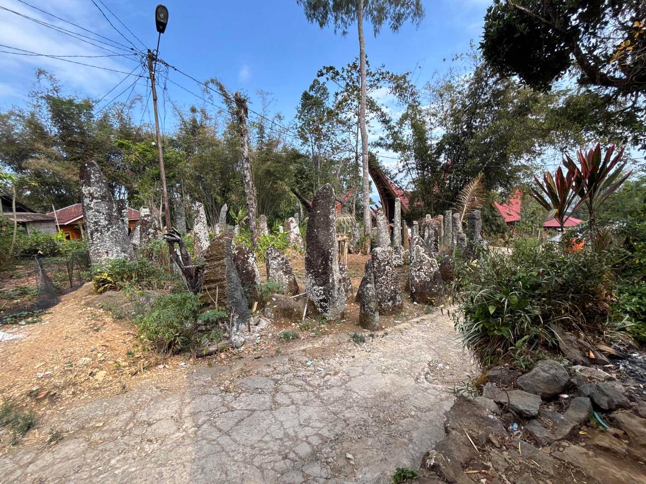 A row of ancient megalithic standing stones lining a path near a traditional village