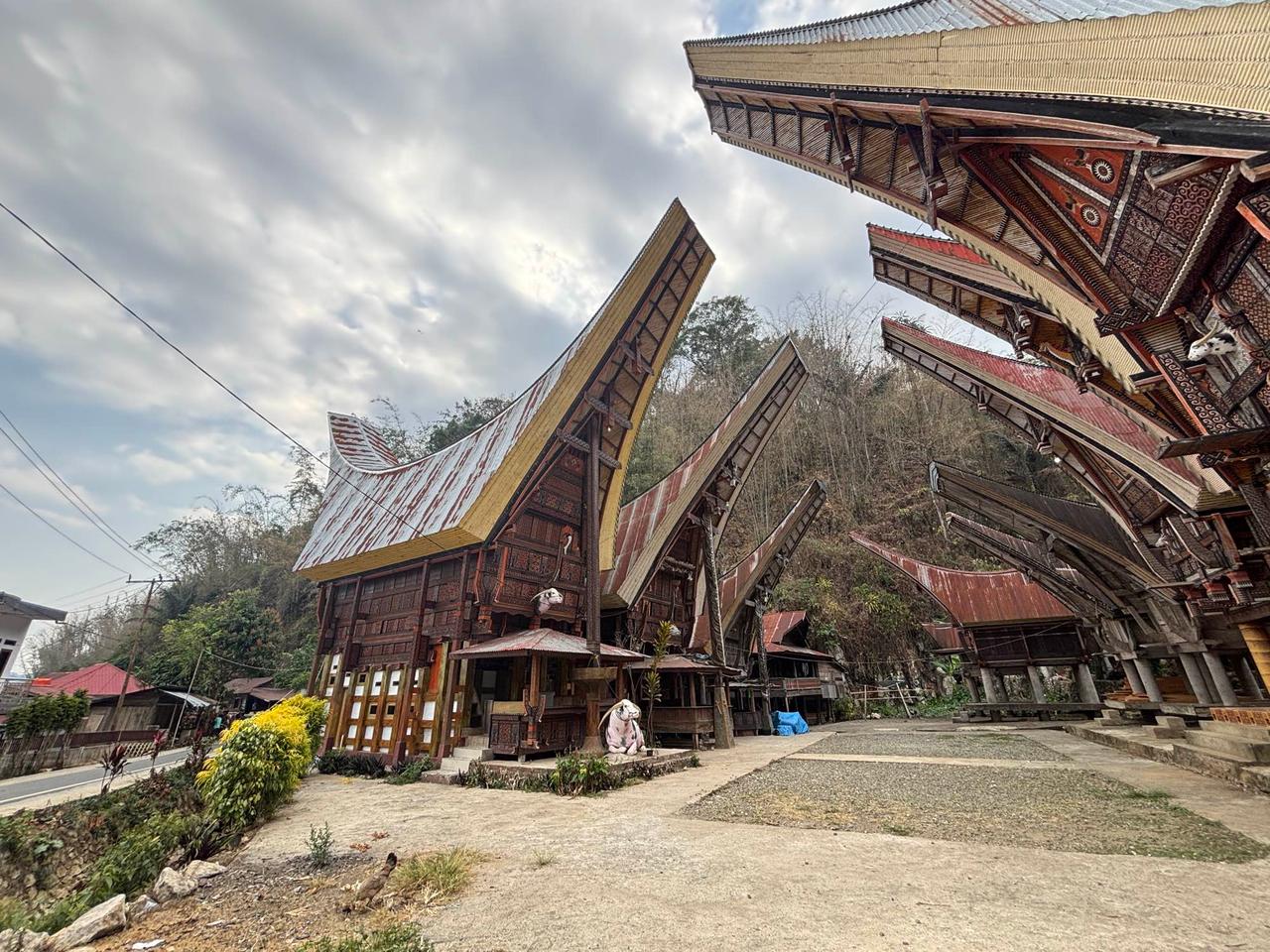 A dramatic low-angle view of Tongkonan houses with soaring saddleback roofs against a cloudy sky