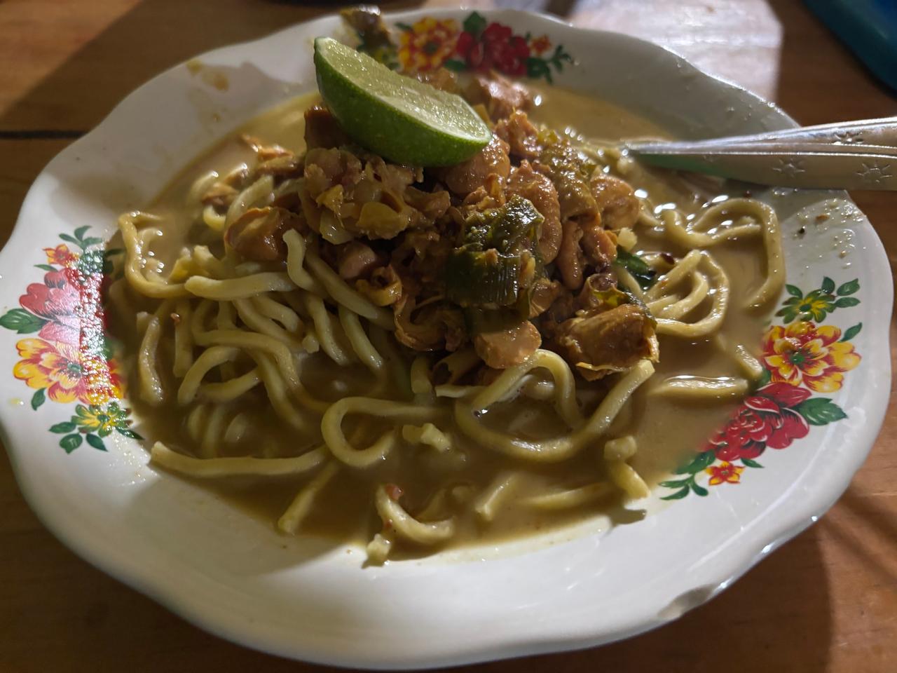 A plate of noodle soup with chicken, peanuts and a lime wedge, eaten at the guesthouse for dinner