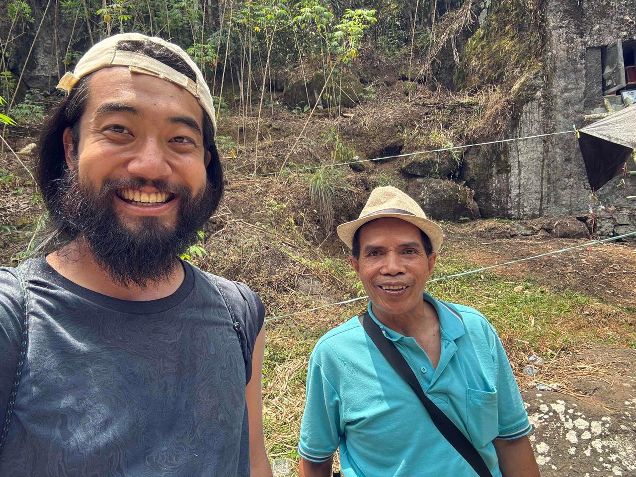 The author smiling alongside a local resident at the gravesite, with the rock tomb visible behind them