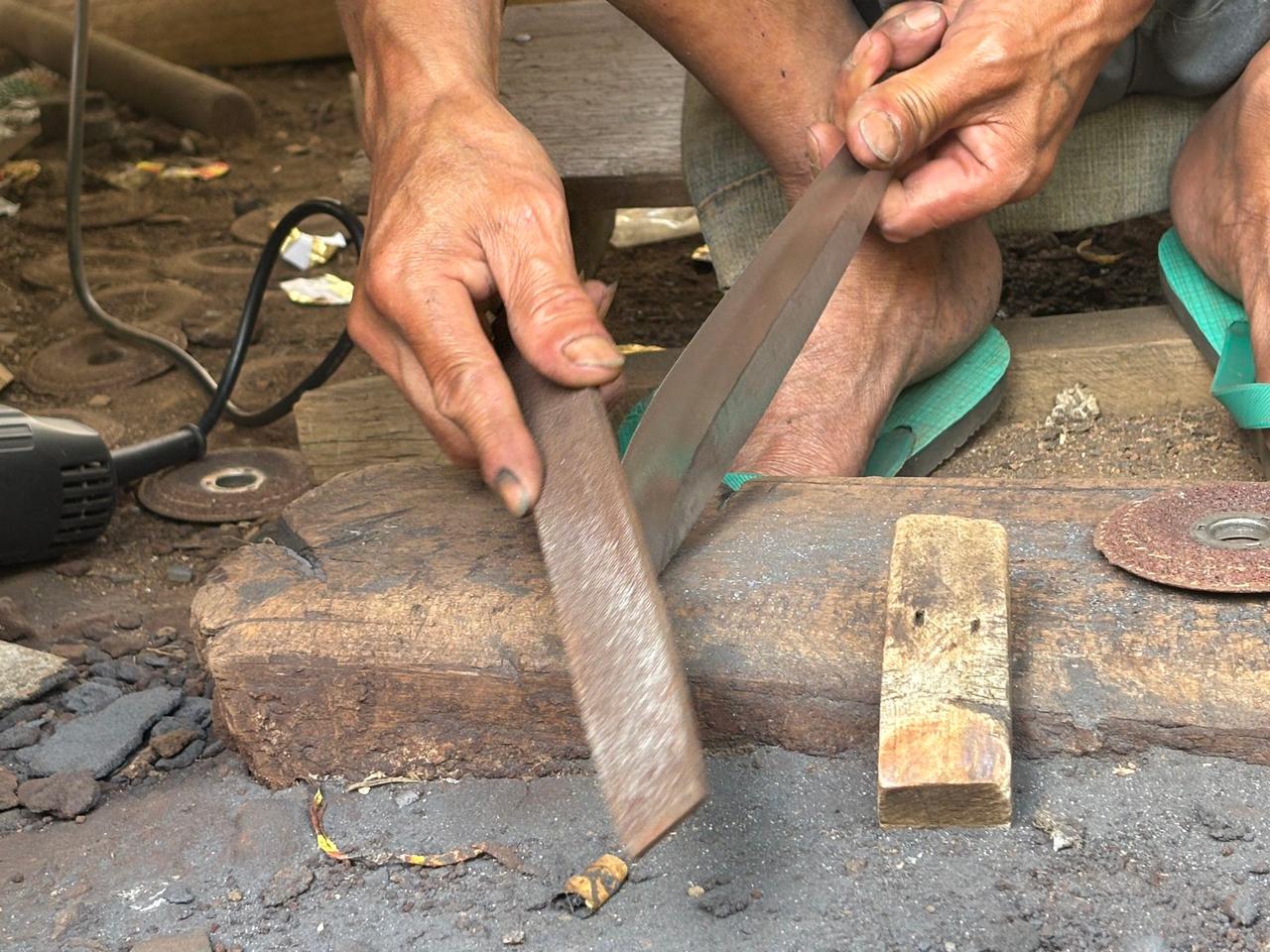 A blacksmith's weathered hands filing the blade of a ceremonial knife by hand