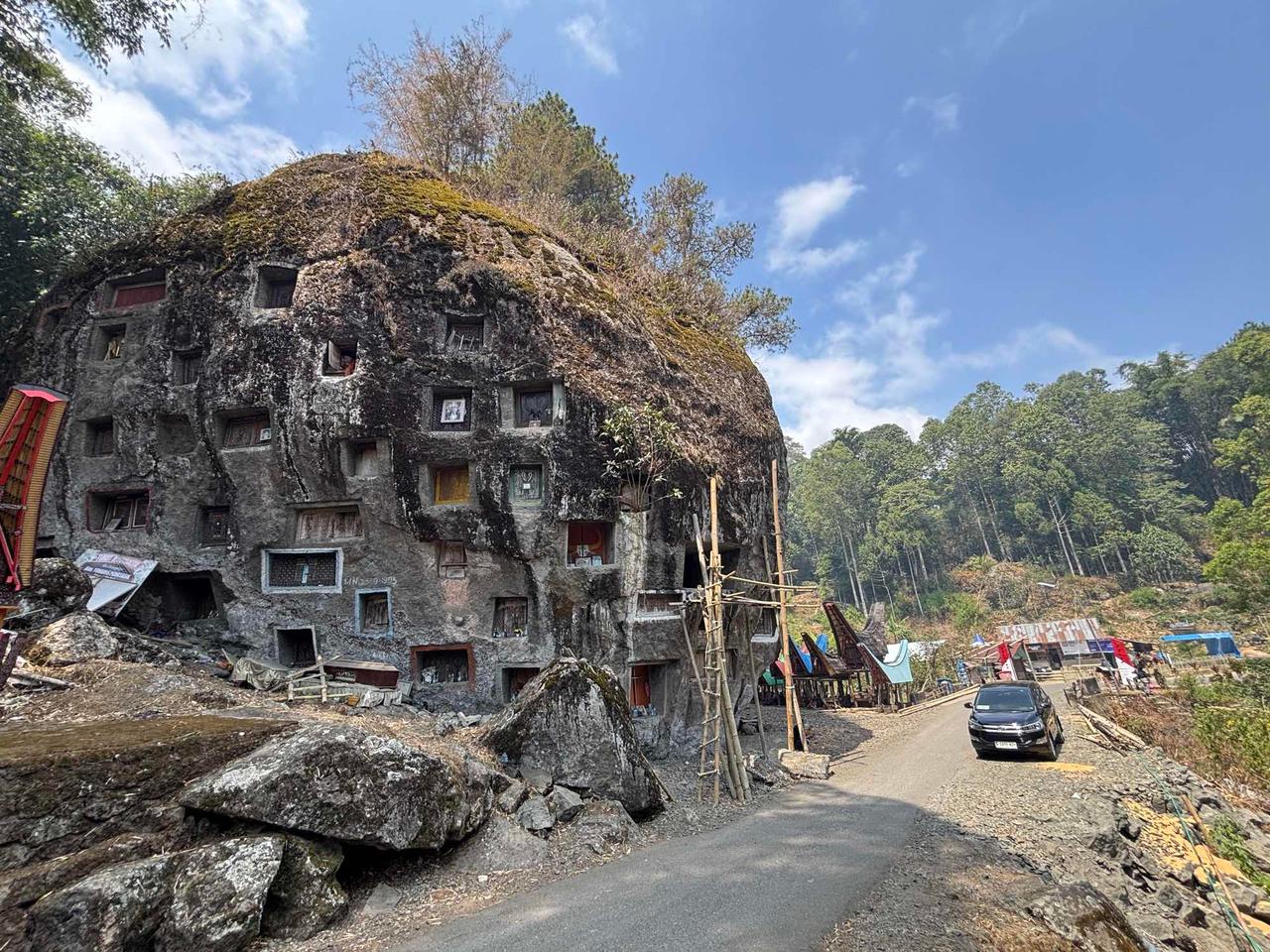 A massive moss-covered rock cliff riddled with carved burial niches at Tonga Riu