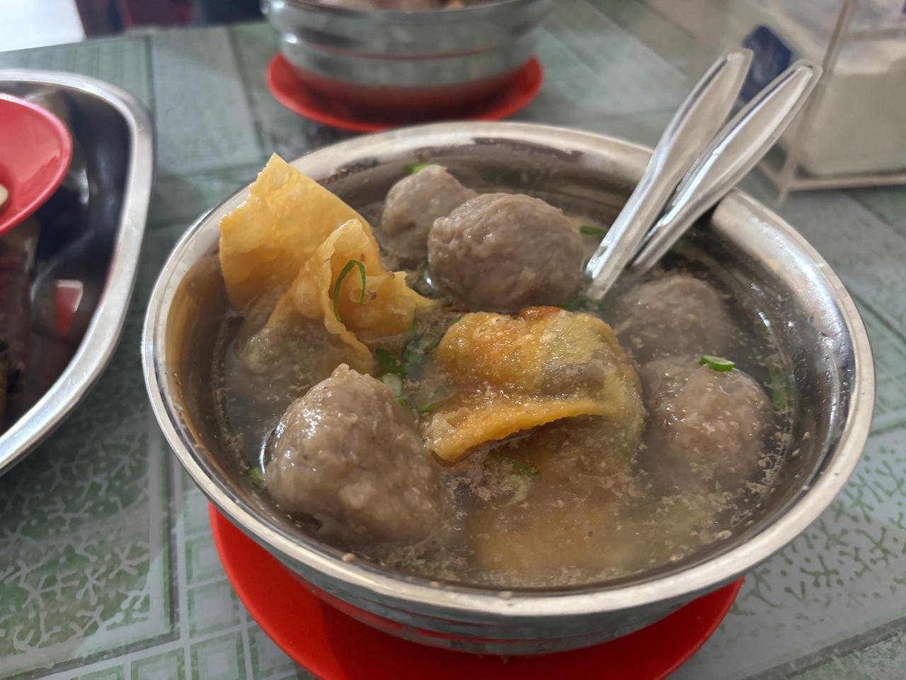 A bowl of meatball soup with wonton crackers and scallions