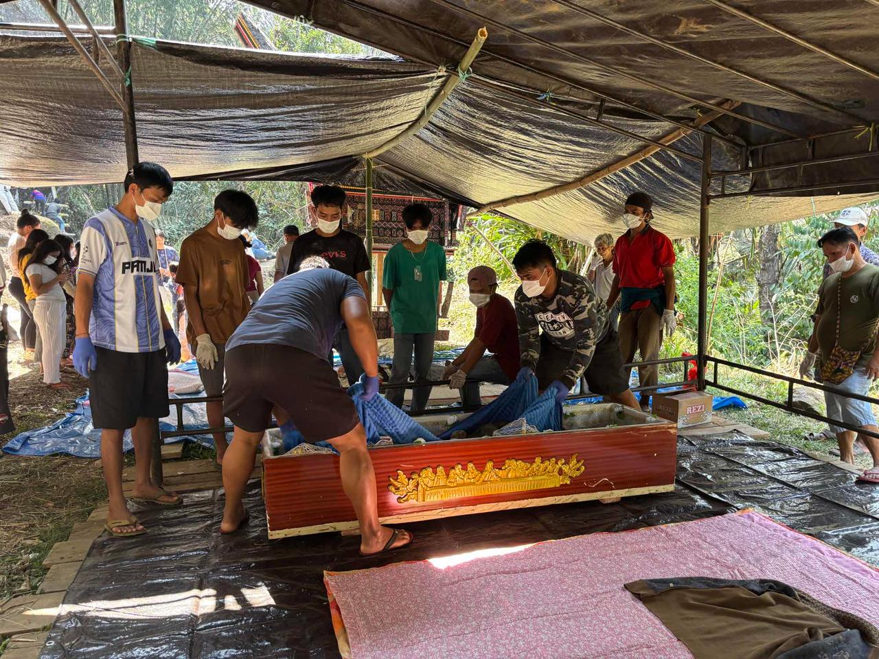 Family members carrying a red lacquered coffin out from beneath a tent shelter