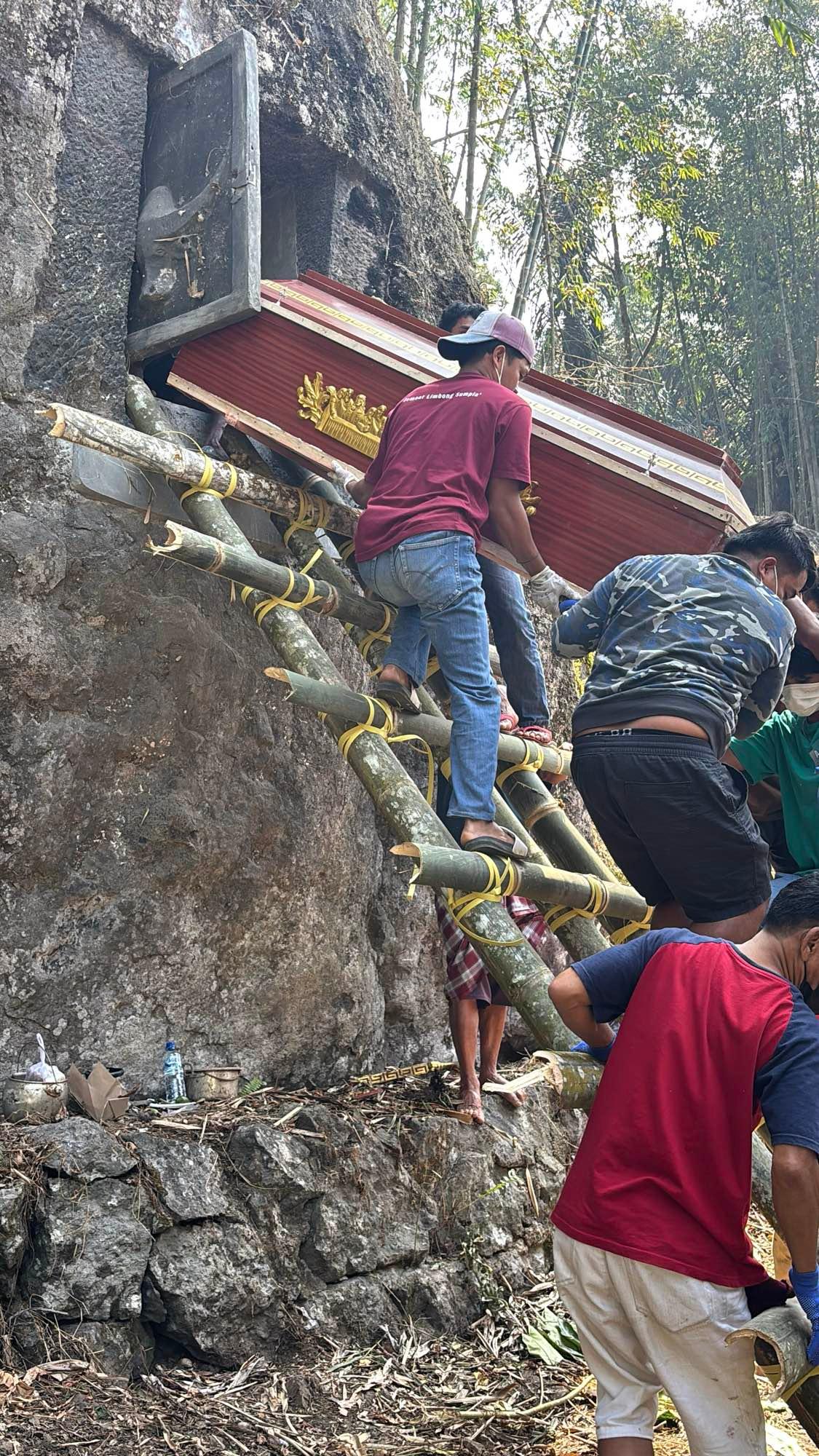 Workers sliding a red lacquered coffin down a bamboo scaffold from a rock tomb