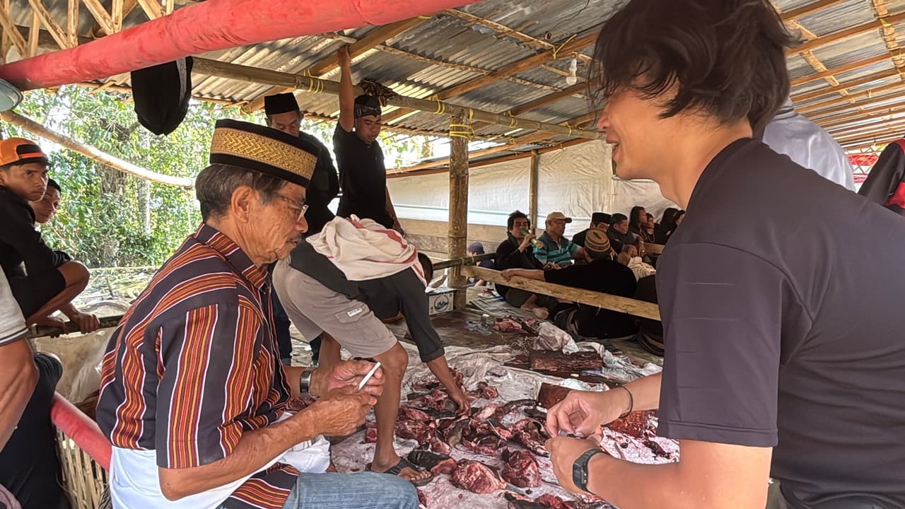 An elder in traditional dress sorting freshly butchered buffalo meat on a table