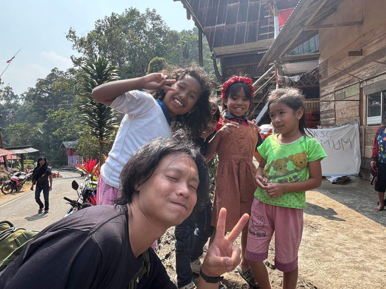 A group photo with laughing local children in front of a traditional wooden house