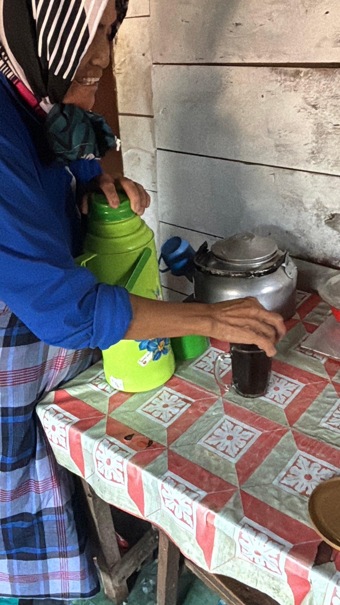 An elderly woman preparing coffee and drinks in a traditional kitchen