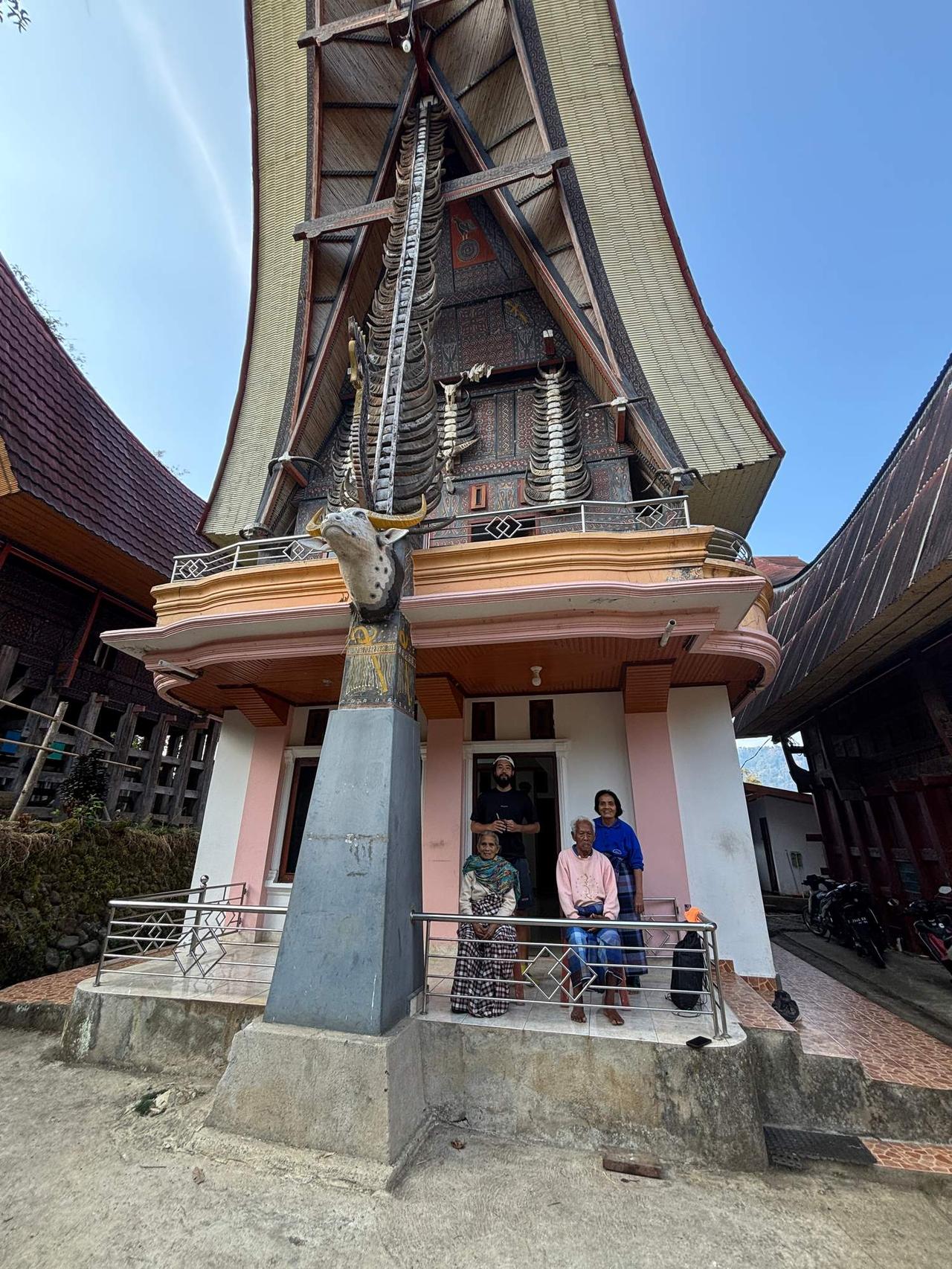 A commemorative group photo with the host family in front of an ornately decorated Tongkonan house