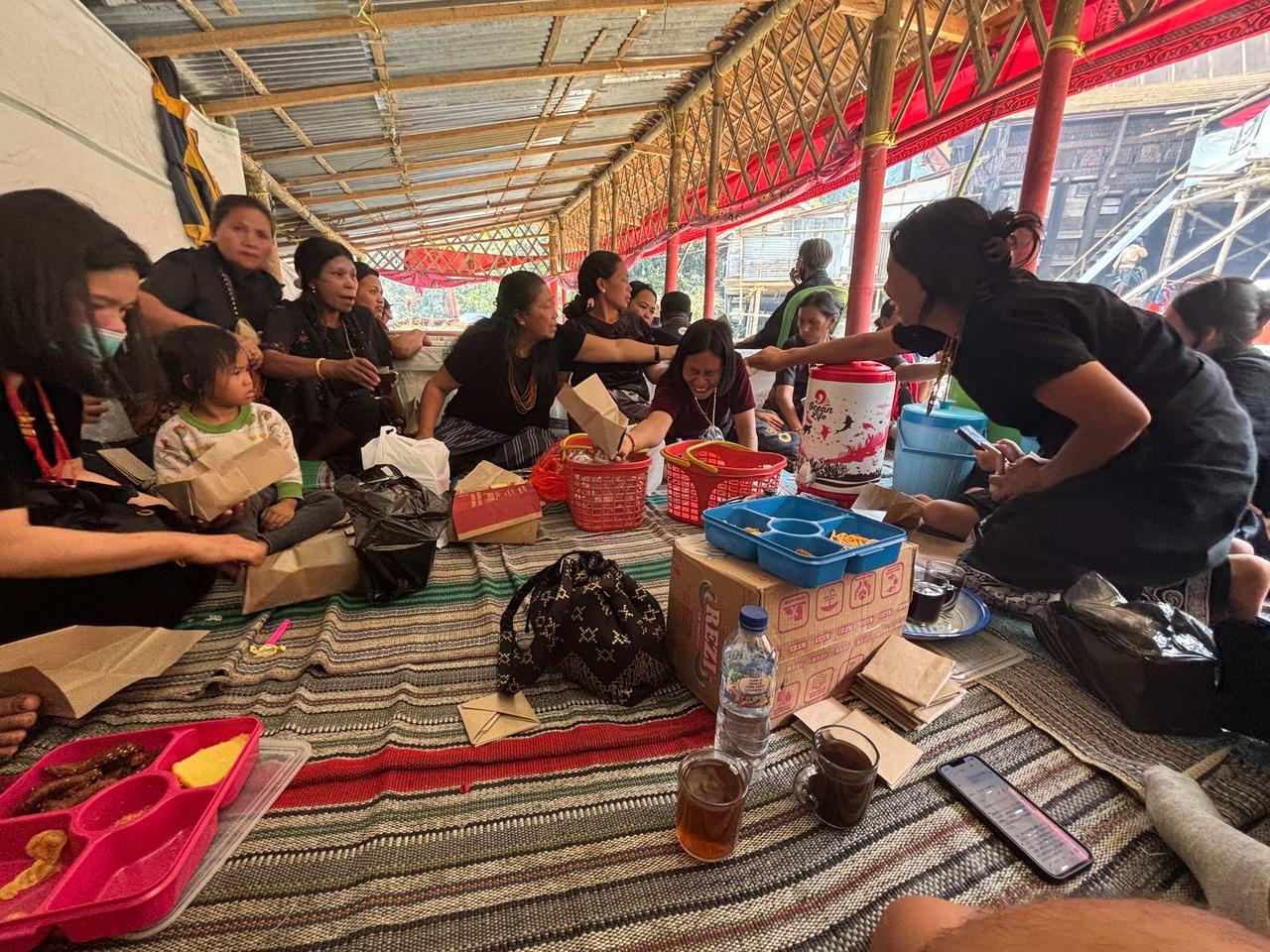A group of local women sharing a communal meal on woven mats under a pavilion