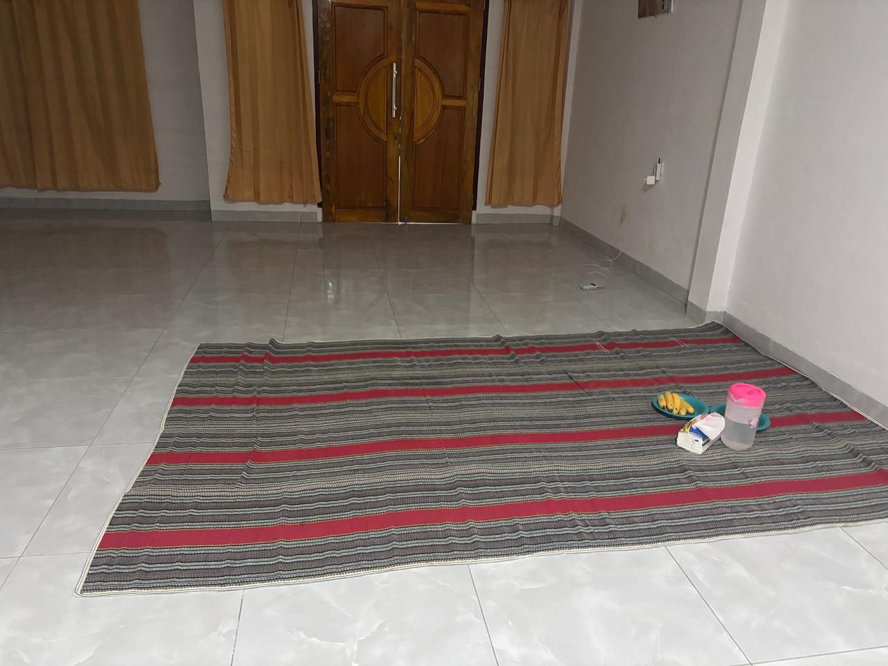 A woven sleeping mat laid out on the tiled floor of a spacious traditional house at night