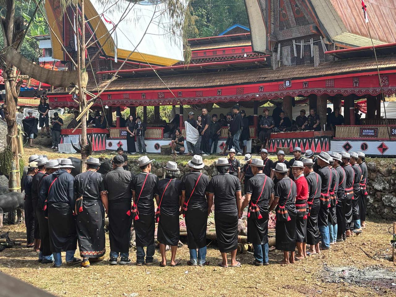 A large circle of men in matching black attire and hats performing the Ma'badong chant