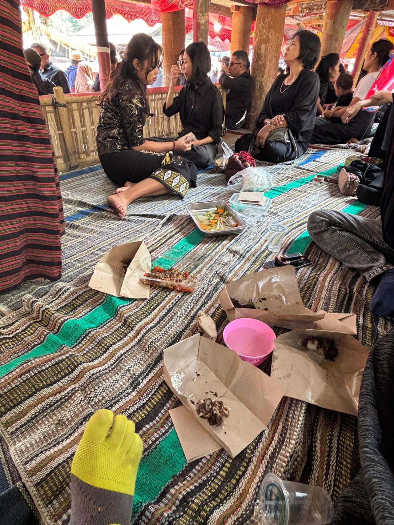A group of locals sitting and talking together on a woven mat under a pavilion