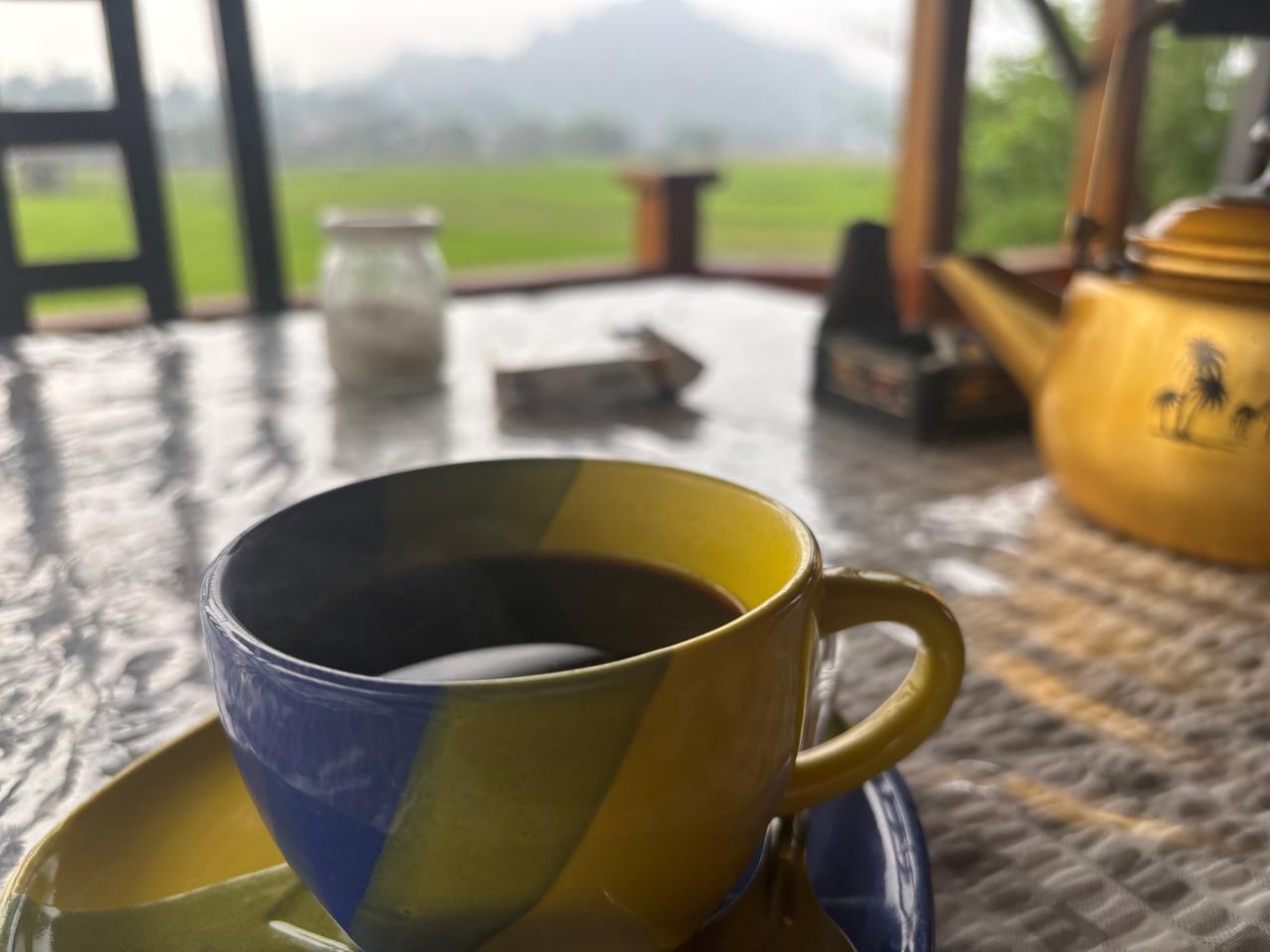 A cup of dark black coffee on a table overlooking misty rice fields and mountains