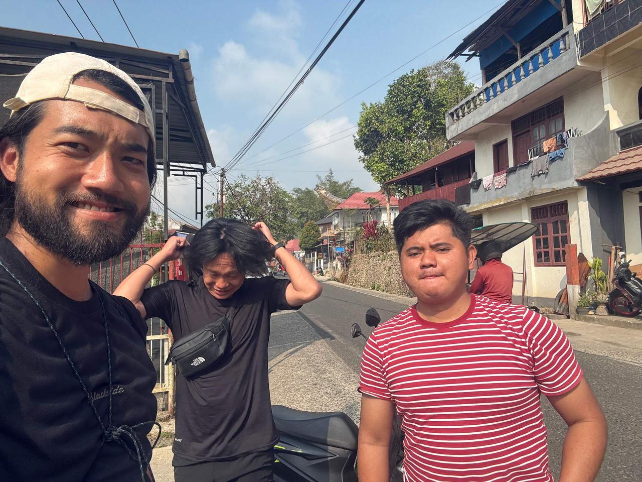 A selfie with friends on a village road, motorbikes parked beside them under a clear blue sky