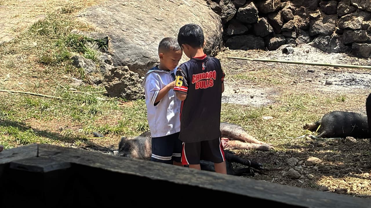 Two young boys standing quietly together at the edge of the ceremony grounds
