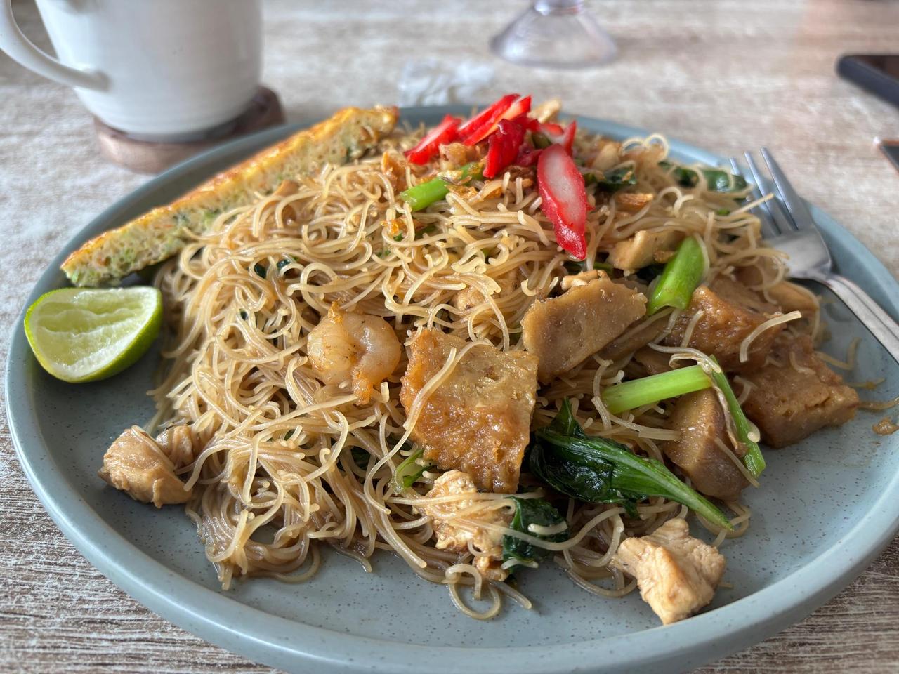 A generous plate of bihun rice noodles with shrimp, tofu, chicken, and chili, served with a wedge of lime