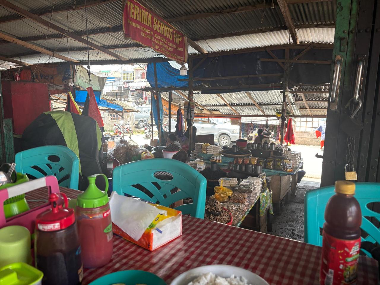 The interior of a roadside warung with plastic chairs and jars of local snacks and coffee