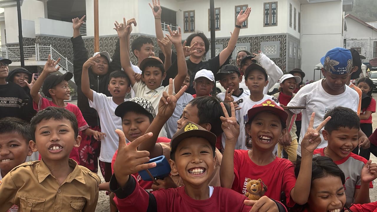 A crowd of laughing children throwing up peace signs and hand gestures in a town square