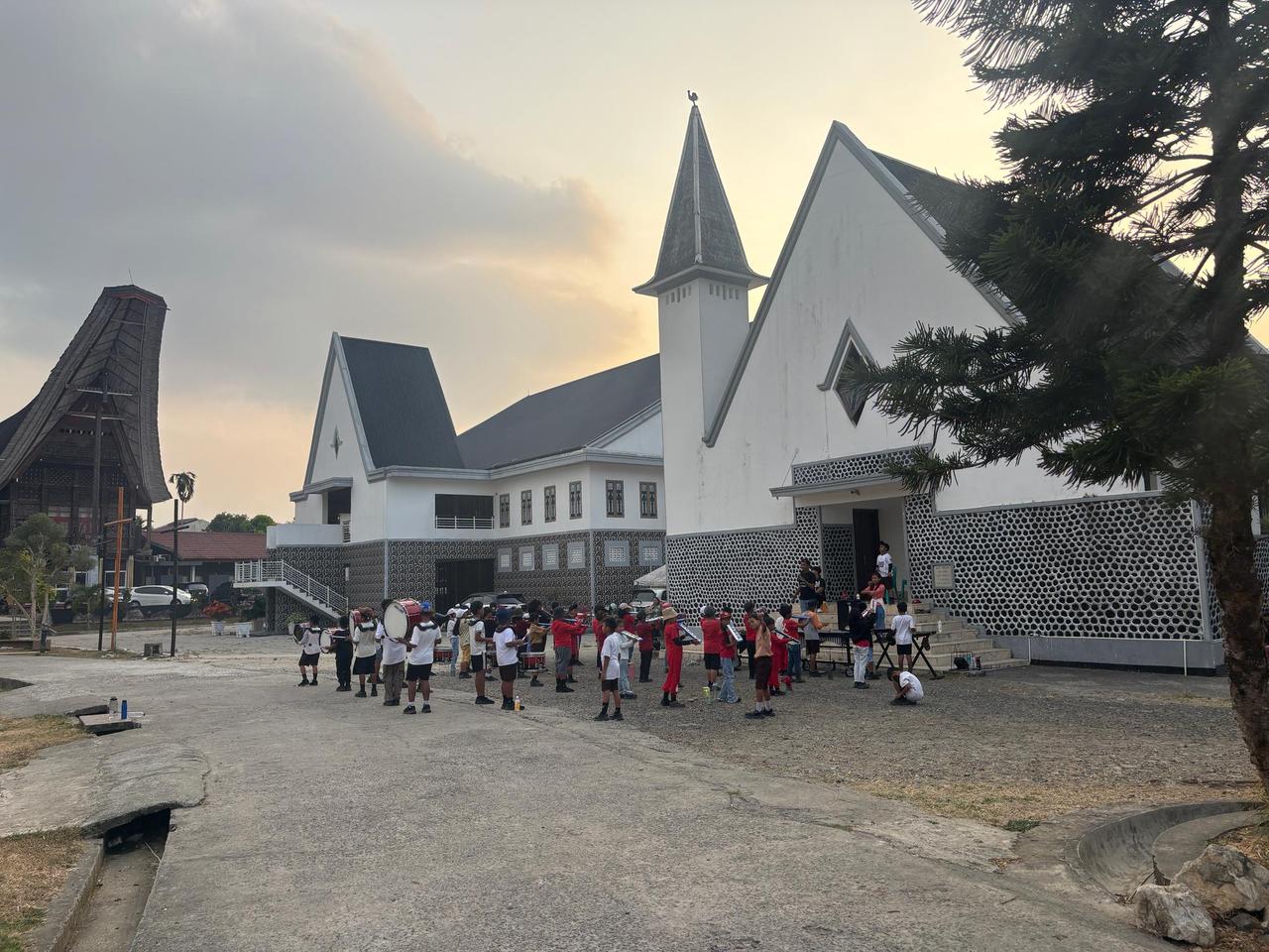 A children's marching band lined up with drums in front of a church at dusk