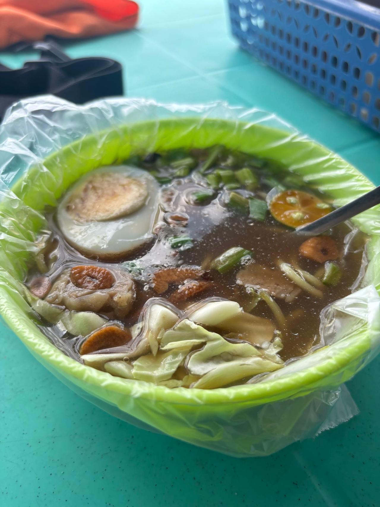 A bowl of mami noodle soup with egg, meat, and vegetables