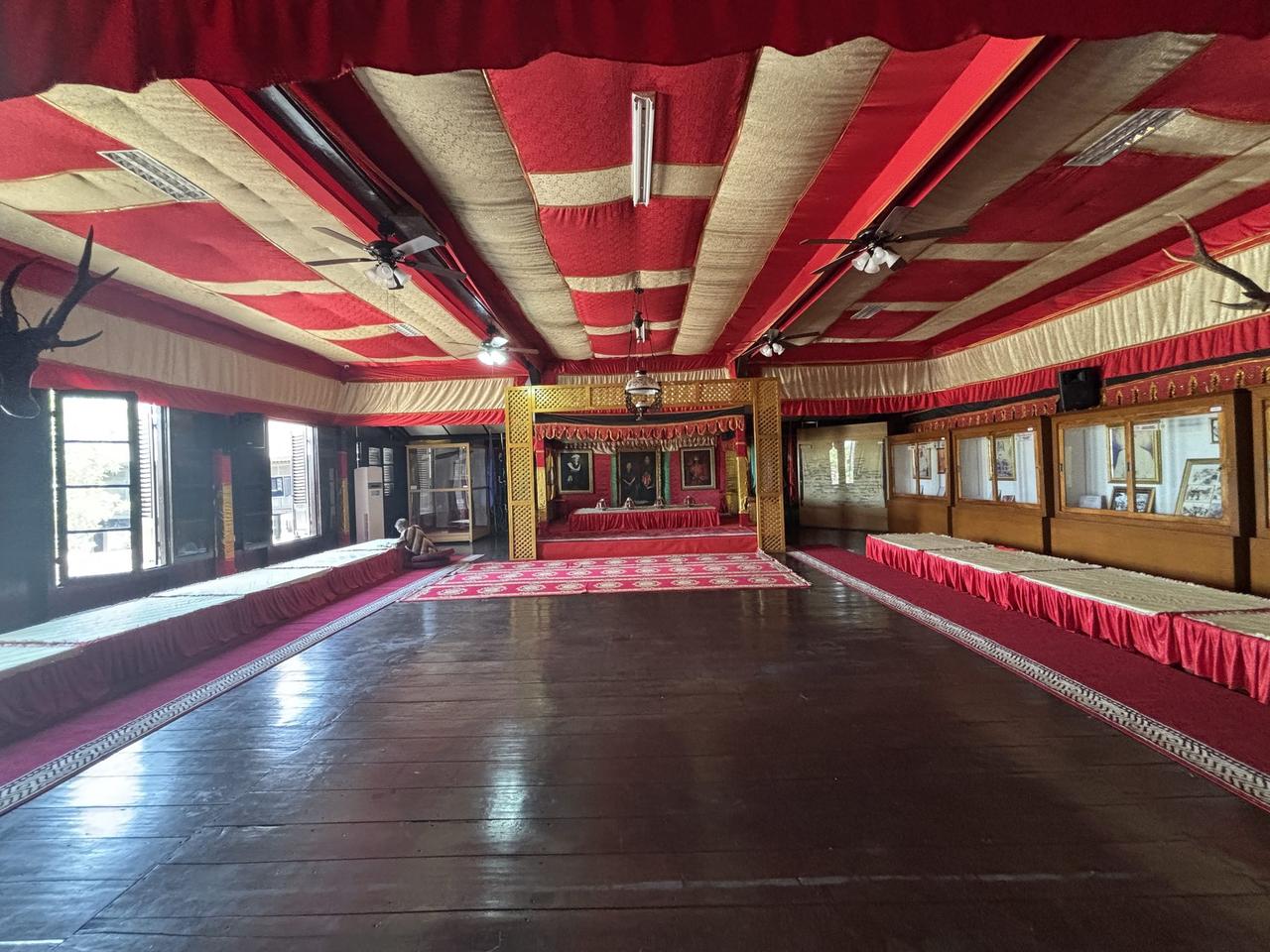 Aula utama istana, langit-langitnya yang merah-emas membingkai sebuah singgasana tinggi berkanopi tempat sang raja dahulu duduk.