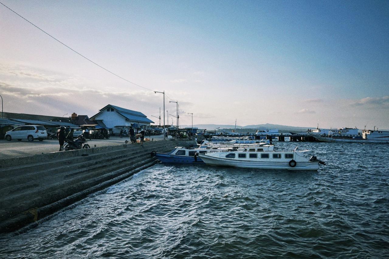 Small boats moored along a pier in Baubau's harbor, a market building visible on the shoreline behind them.