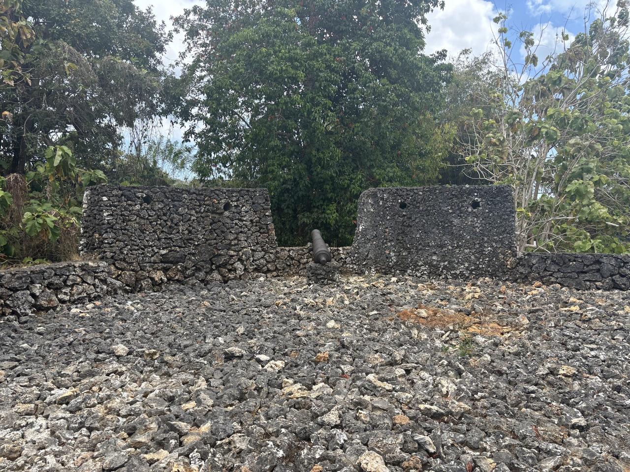 A stone bastion wall with an old cannon positioned between two coral-limestone sections at Benteng Keraton Buton.