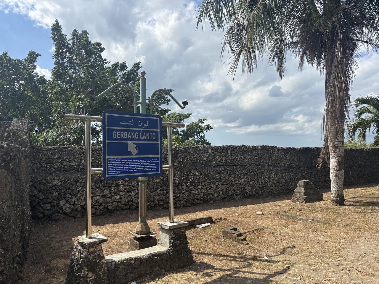 The Gerbang Lanto sign marking one of the twelve named gates of Benteng Keraton Buton, with the coral-stone perimeter wall behind it.