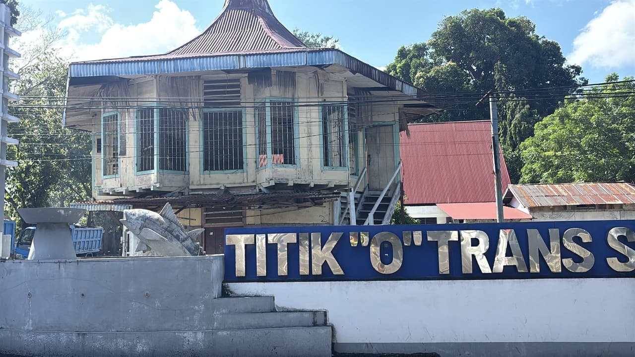 An old wooden building on stilts beside a Titik Nol monument marking the entrance to the fishing village near the Bitung fish market.