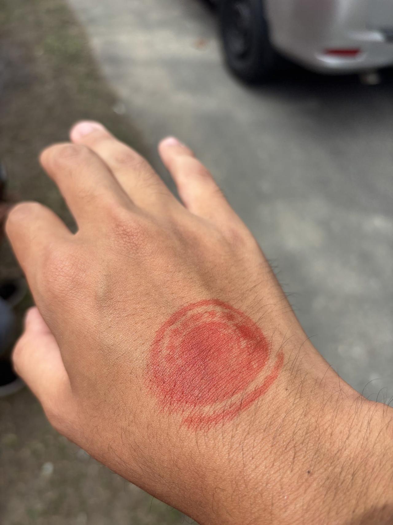 A red circular entry stamp on the back of a hand, given to attendees who paid the entrance fee at Festival Marawai.