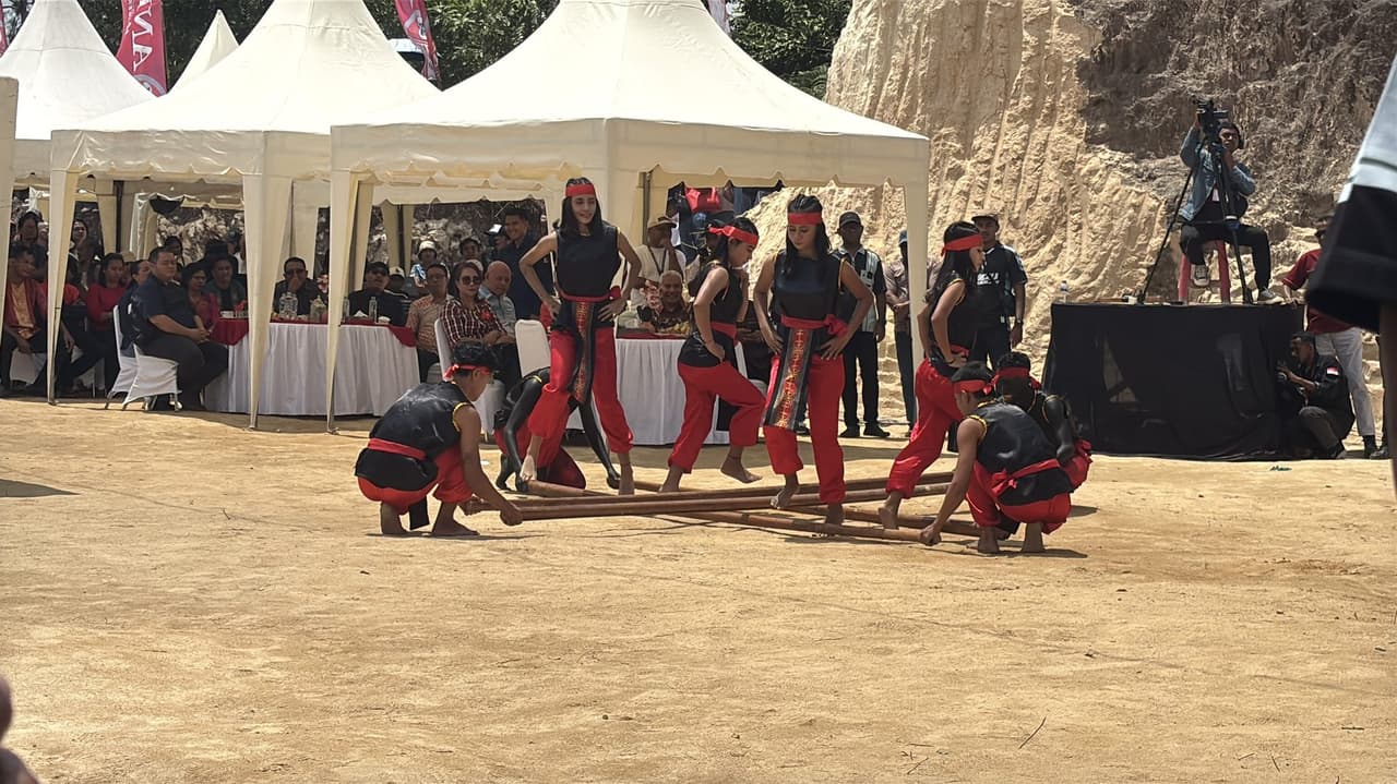 Dancers in black and red performing tari saureka-reka, jumping between bamboo poles clapped in rhythm by a team on the ground at Festival Marawai.