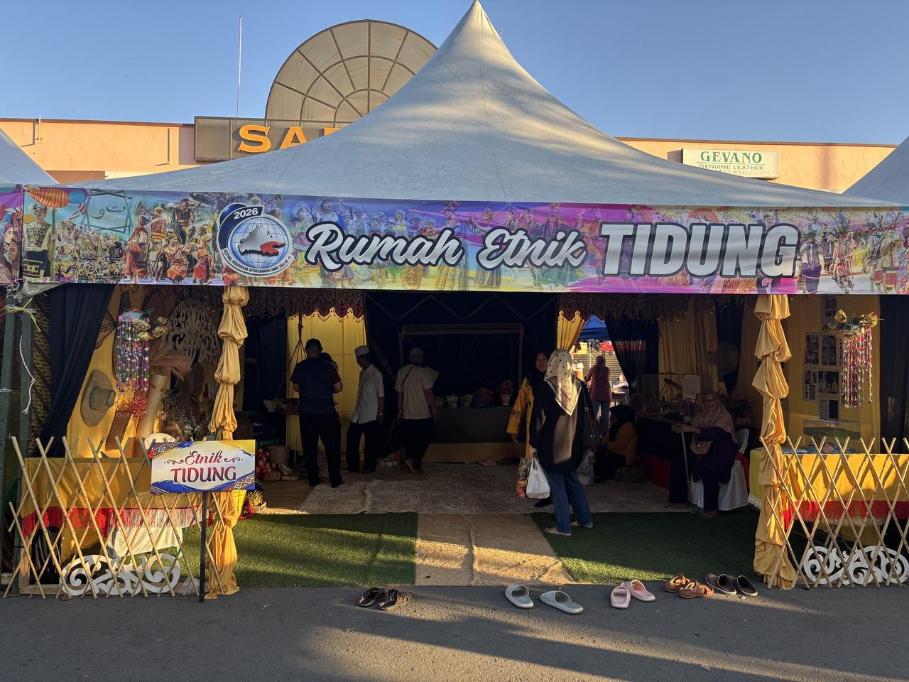 The exterior of the Rumah Etnik Tidung tent, decorated with a large festival banner, sandals lined up outside the entrance.