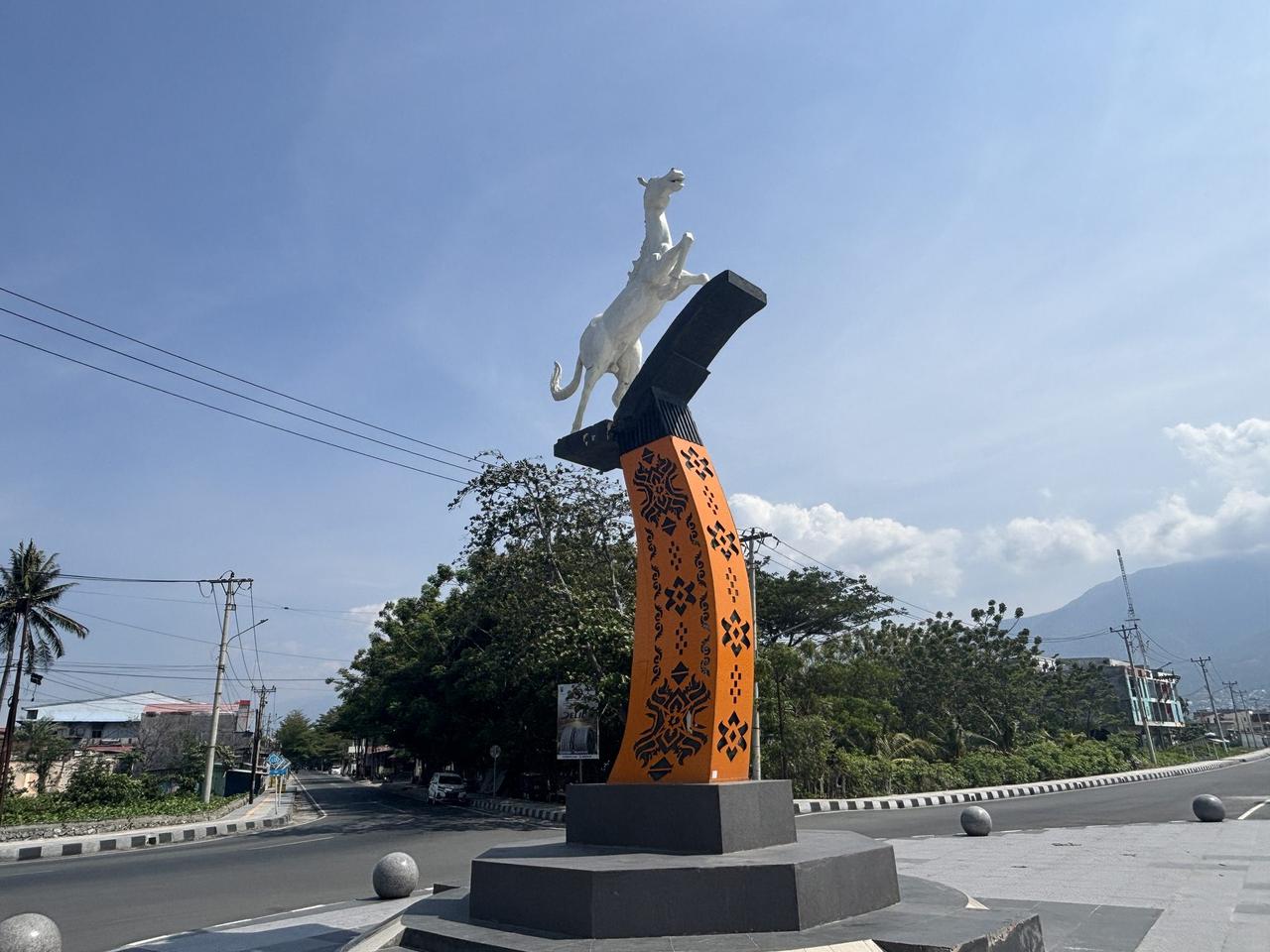 Patung kuda putih yang sedang melompat di atas alas berpola di sebuah bundaran jalan di Palu.