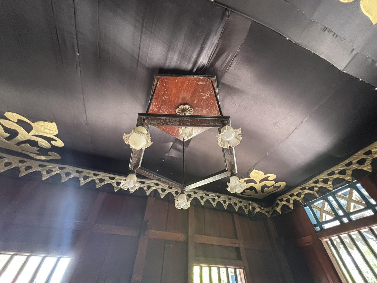 Lampu langit-langit berbentuk pentagon yang megah, terpasang berlatar hiasan atap emas berukir di dalam istana.