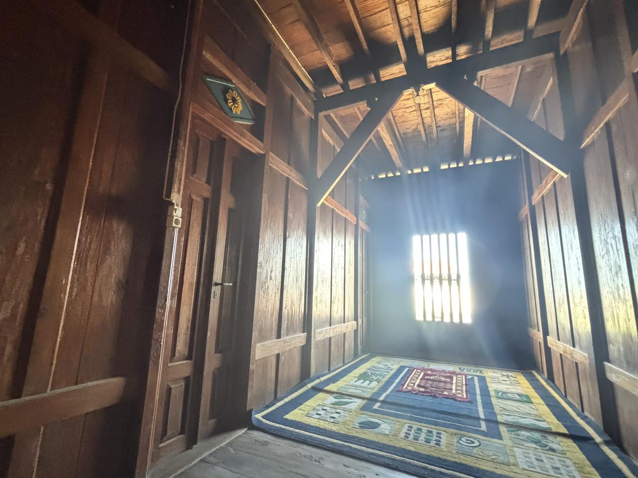 Ruangan berlantai atas berdinding kayu dengan permadani bermotif terhampar di lantainya.