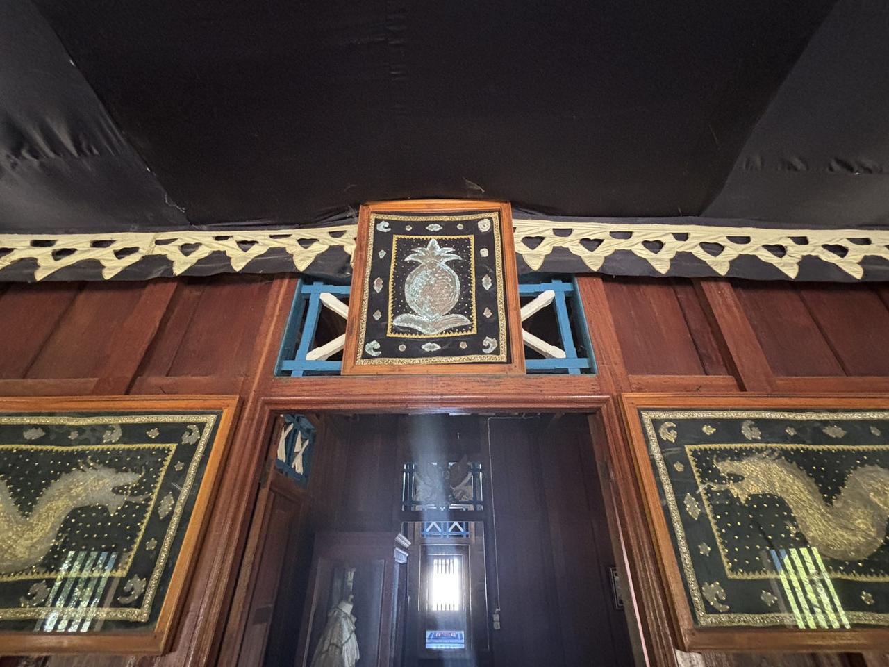 Panel sulaman menampilkan motif nanas yang diapit dua panel naga emas di atas sebuah ambang pintu.