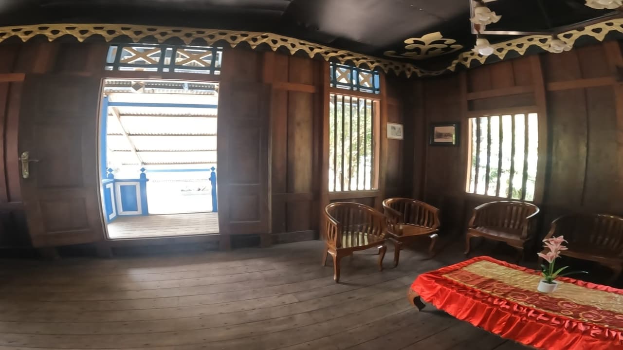 Ruang penerimaan tamu di dalam istana dengan kursi-kursi kayu berukir, taplak meja merah, dan foto-foto lama di dinding.