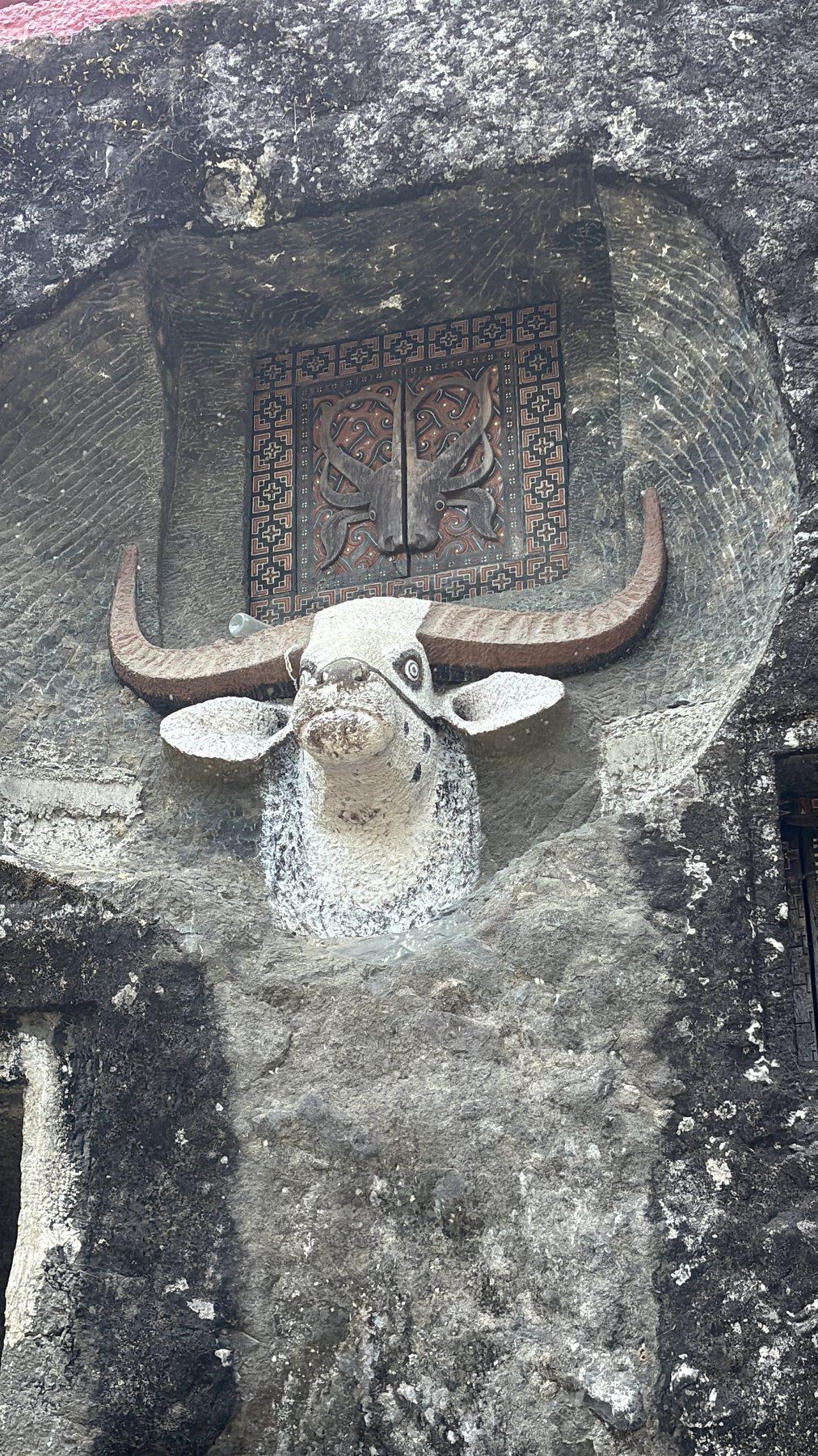 A sculpted buffalo head mounted directly onto the boulder's surface above a carved wooden panel.