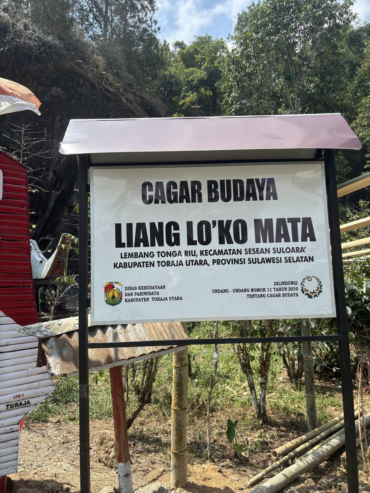 A sign reading Cagar Budaya Liang Lo'ko Mata marking the entrance to the site in Lembang Tonga Riu, Toraja Utara.
