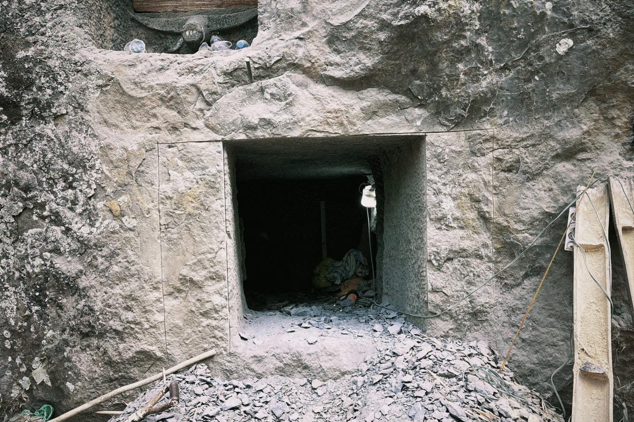 The near-square opening of a chamber currently being carved at the workshop, with wiring and a hanging light visible above it.