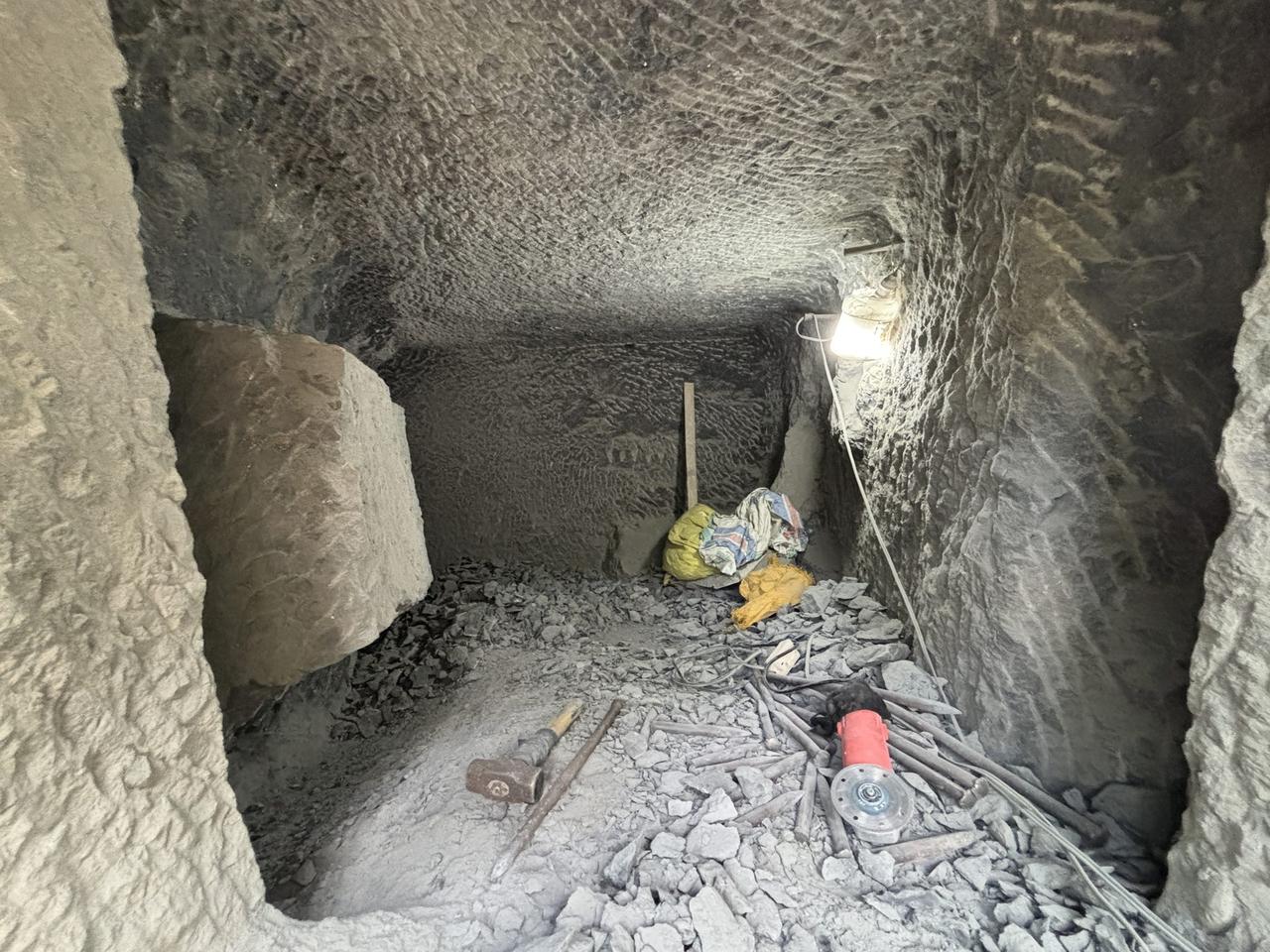 The rough-cut interior of a chamber in progress, stone chips covering the floor around scattered hand tools.
