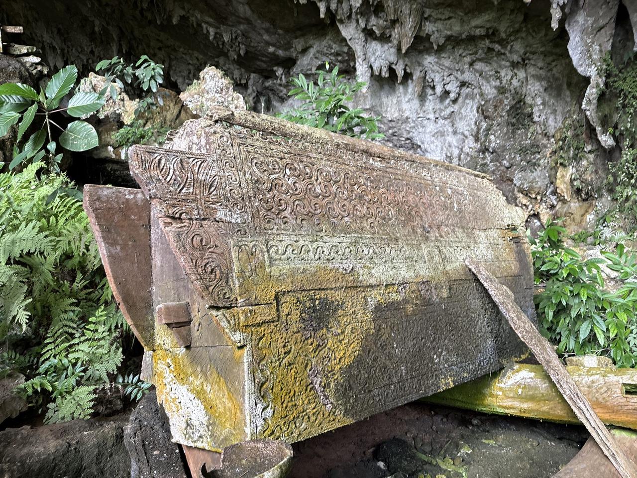 An ornately carved wooden erong coffin panel, its scrollwork still visible after centuries in the cave.